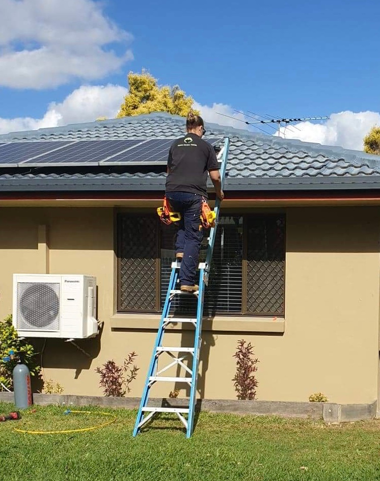 Person ascending a ladder to a residential roof for installation or maintenance work.