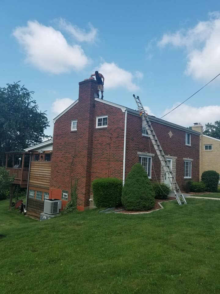 Worker on brick chimney using an extension ladder for roof maintenance, demonstrating ladder safety precautions.