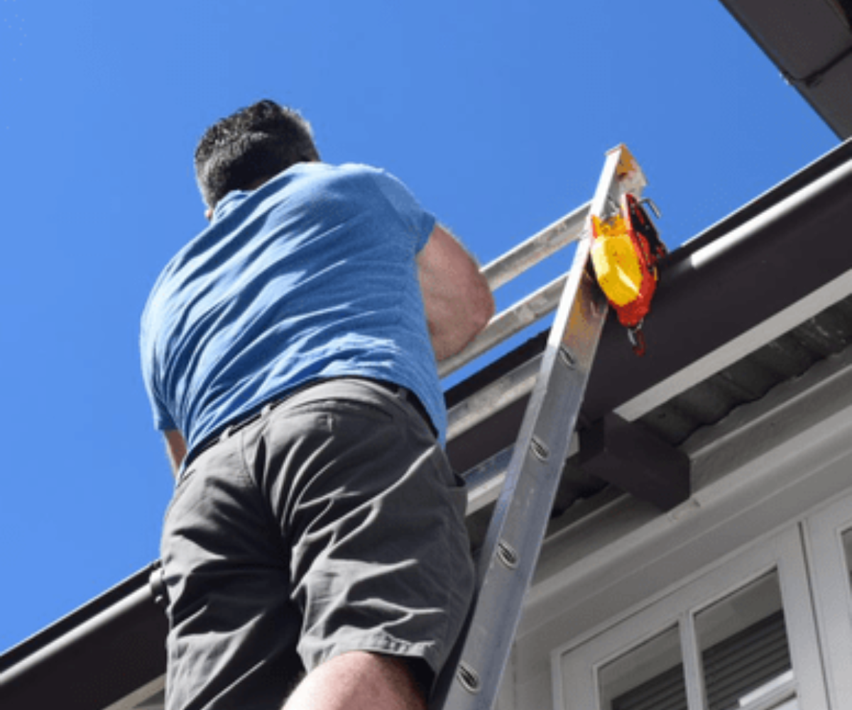 Man climbing a ladder secured with a Lock Jaw Ladder Grip, enhancing safety for rooftop access and preventing ladder movement.
