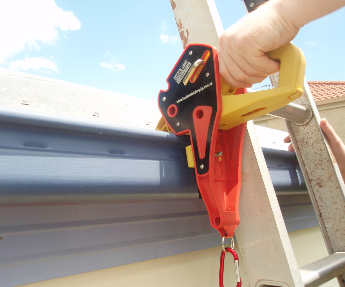 Person using a Lock Jaw Ladder Grip to secure a ladder against a gutter, demonstrating ladder safety.