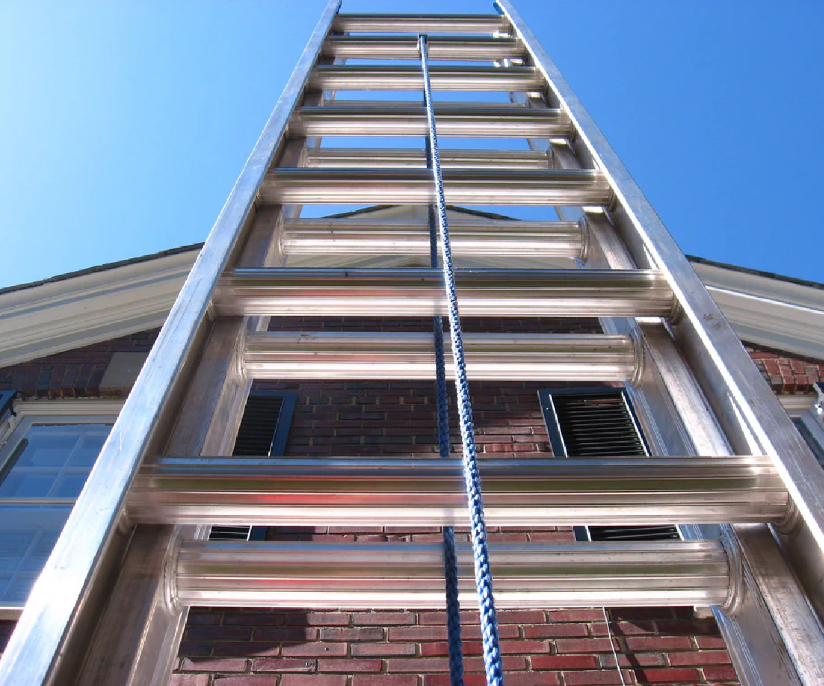 Aluminum extension ladder against a brick building, with a blue rope running its length, under a clear blue sky.