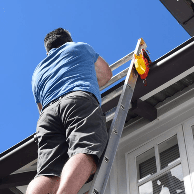 A person is climbing a ladder that's leaning against the roof of a house. A Lock Jaw Ladder Grip is attached to the ladder.