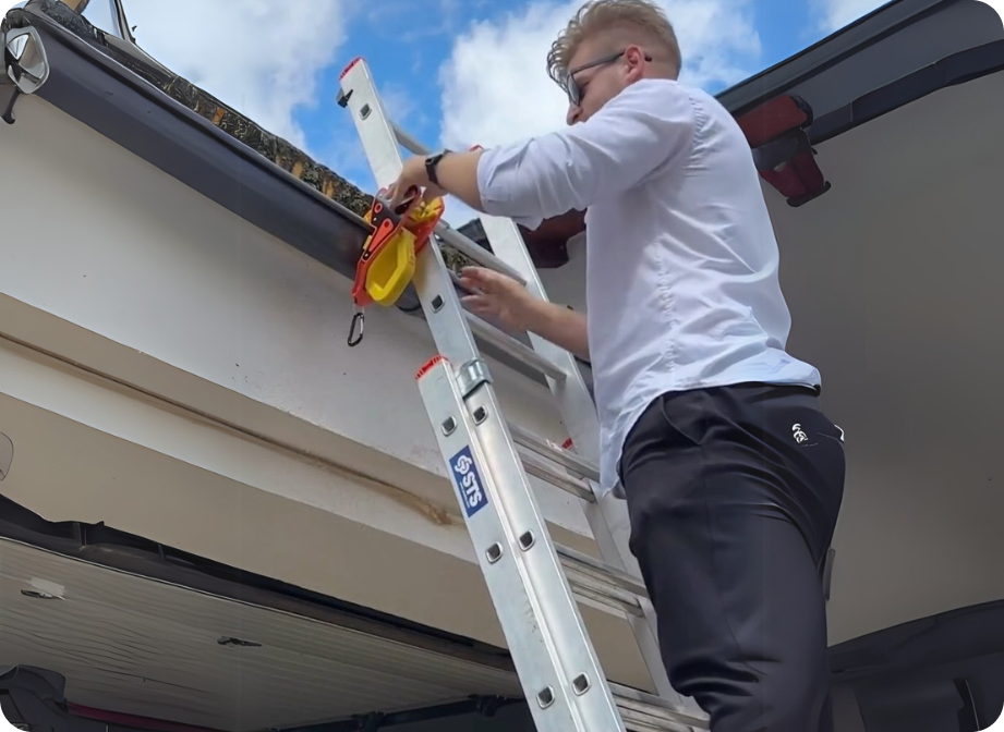 Man in white shirt on an extension ladder, using a tool on what appears to be a boat or RV.