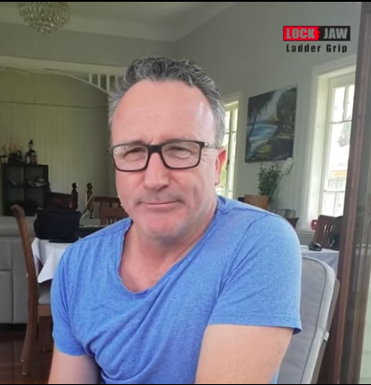 A man with glasses, wearing a blue shirt, is in a room with a Lock Jaw Ladder Grip logo.