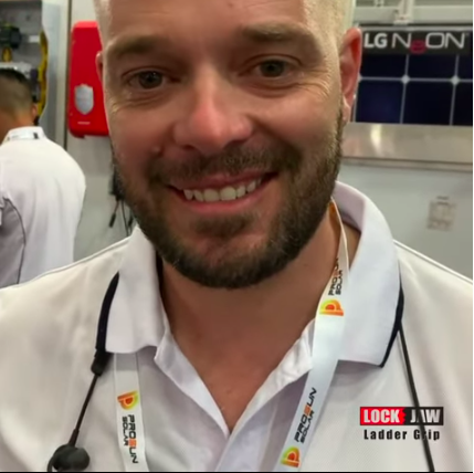 A smiling man with a beard stands next to a ladder with a Lock Jaw Ladder Grip. The text "LGN ON" is visible in the background.