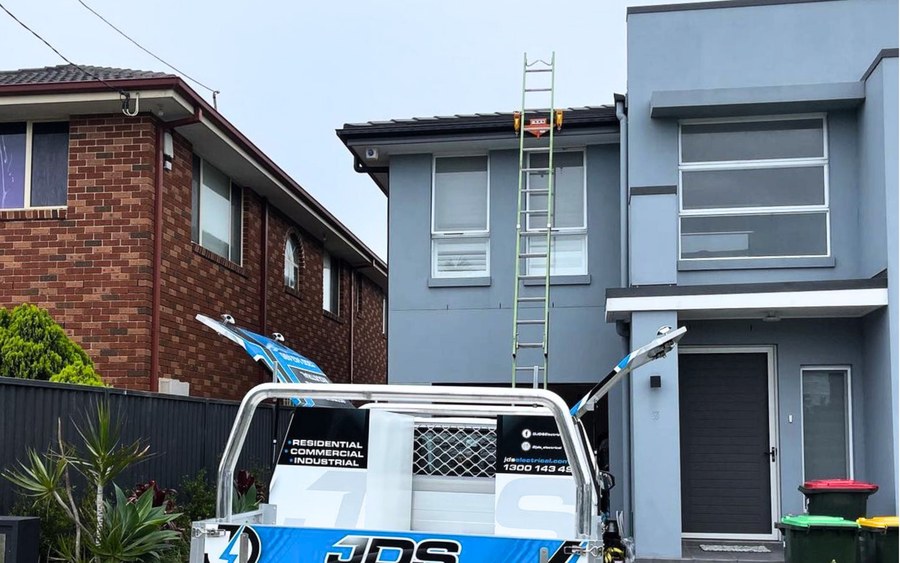 Electrical ute in a driveway, extension ladder up to the gutter of a two-storey house with a Lock Jaw grip at the gutter