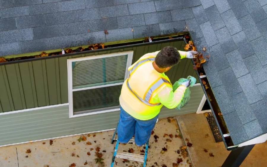 Gutter cleaner working a residential roofline from a ladder set at the eave