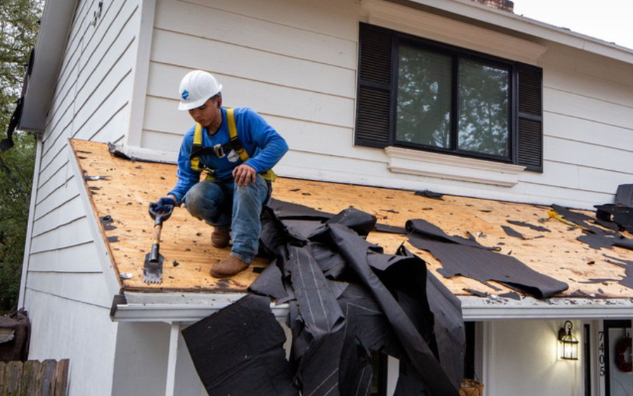 Inspector on a storm-damaged roof section assessing stripped roofing