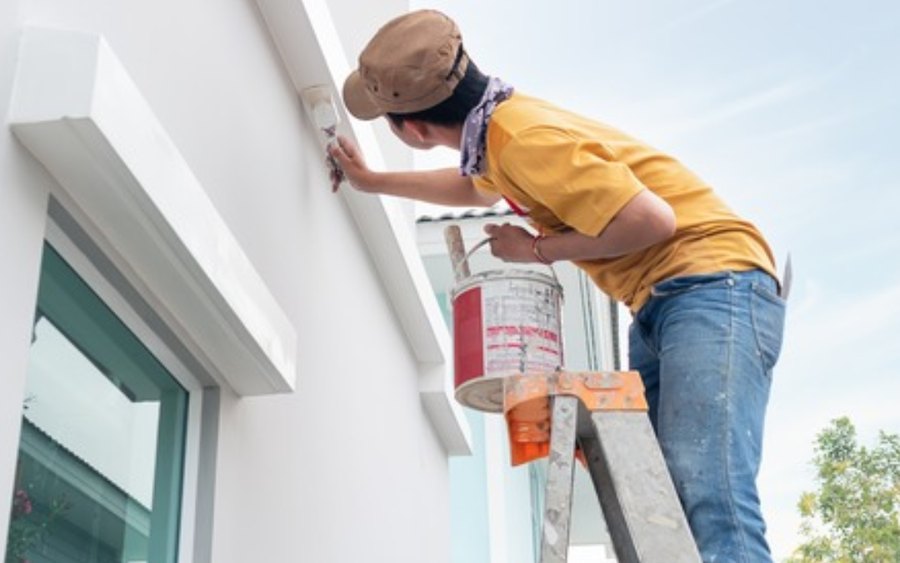 Painter cutting in high on a rendered wall from a ladder
