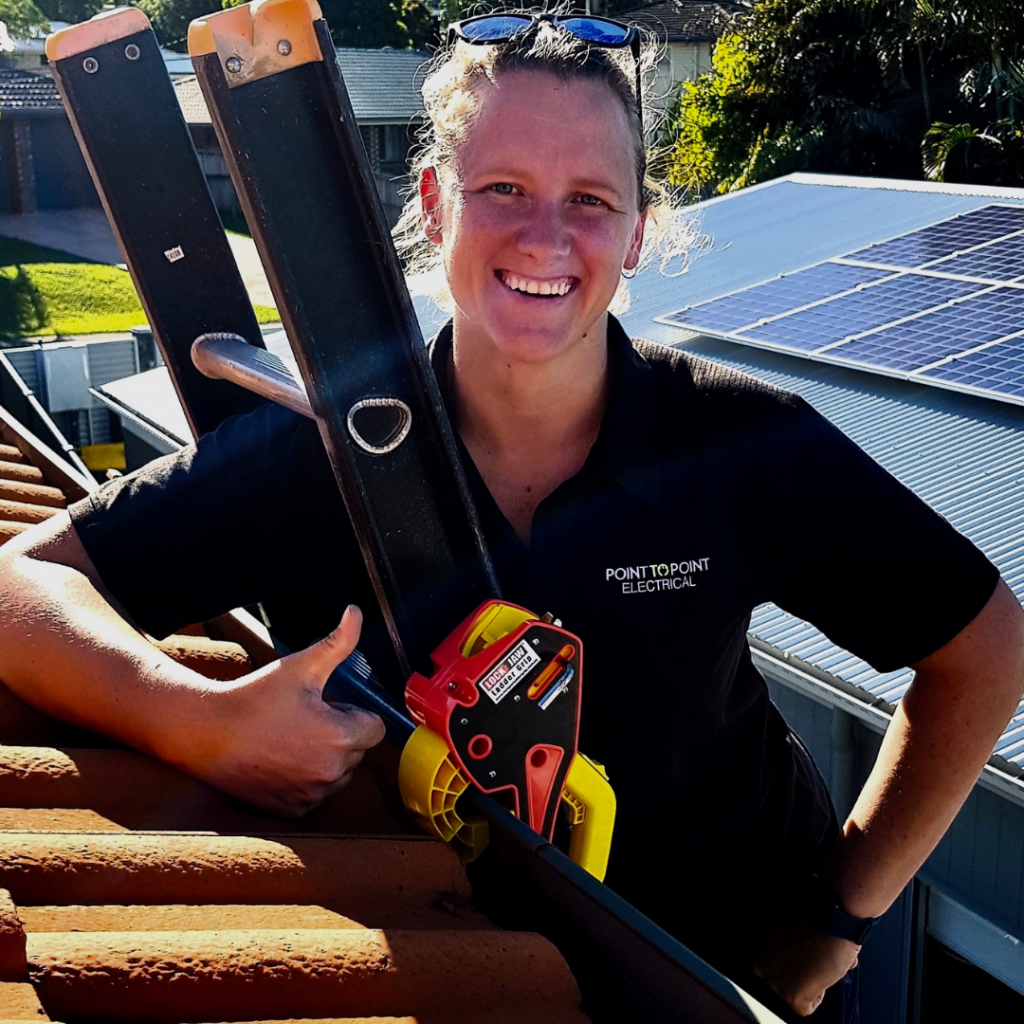Electrician smiling while using Lock Jaw Ladder Grip for safe roof access on a sunny day with solar panels in the background.