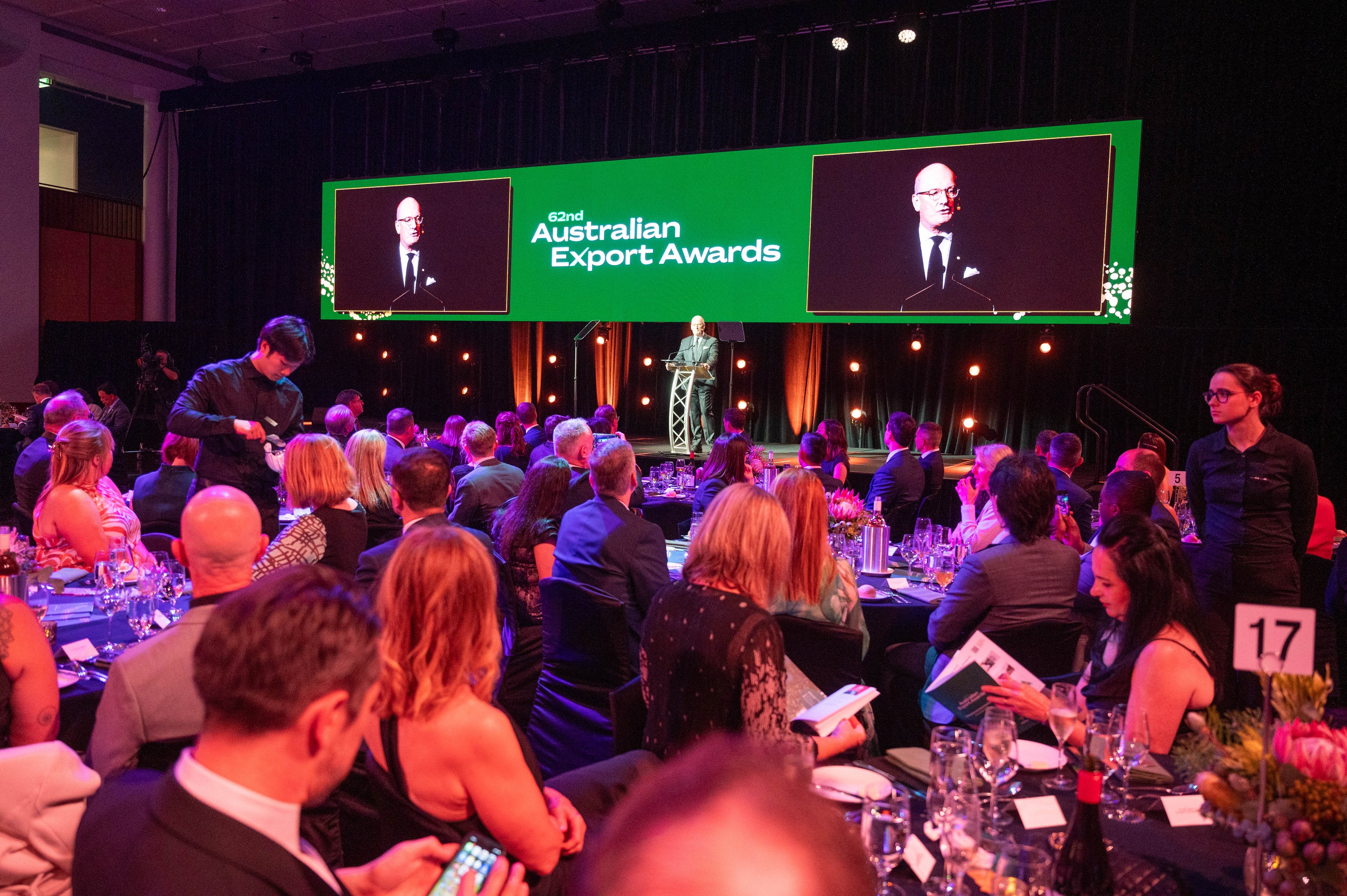 Audience at gala dinner watches speaker on stage at 62nd Australian Export Awards, with large screens overhead.