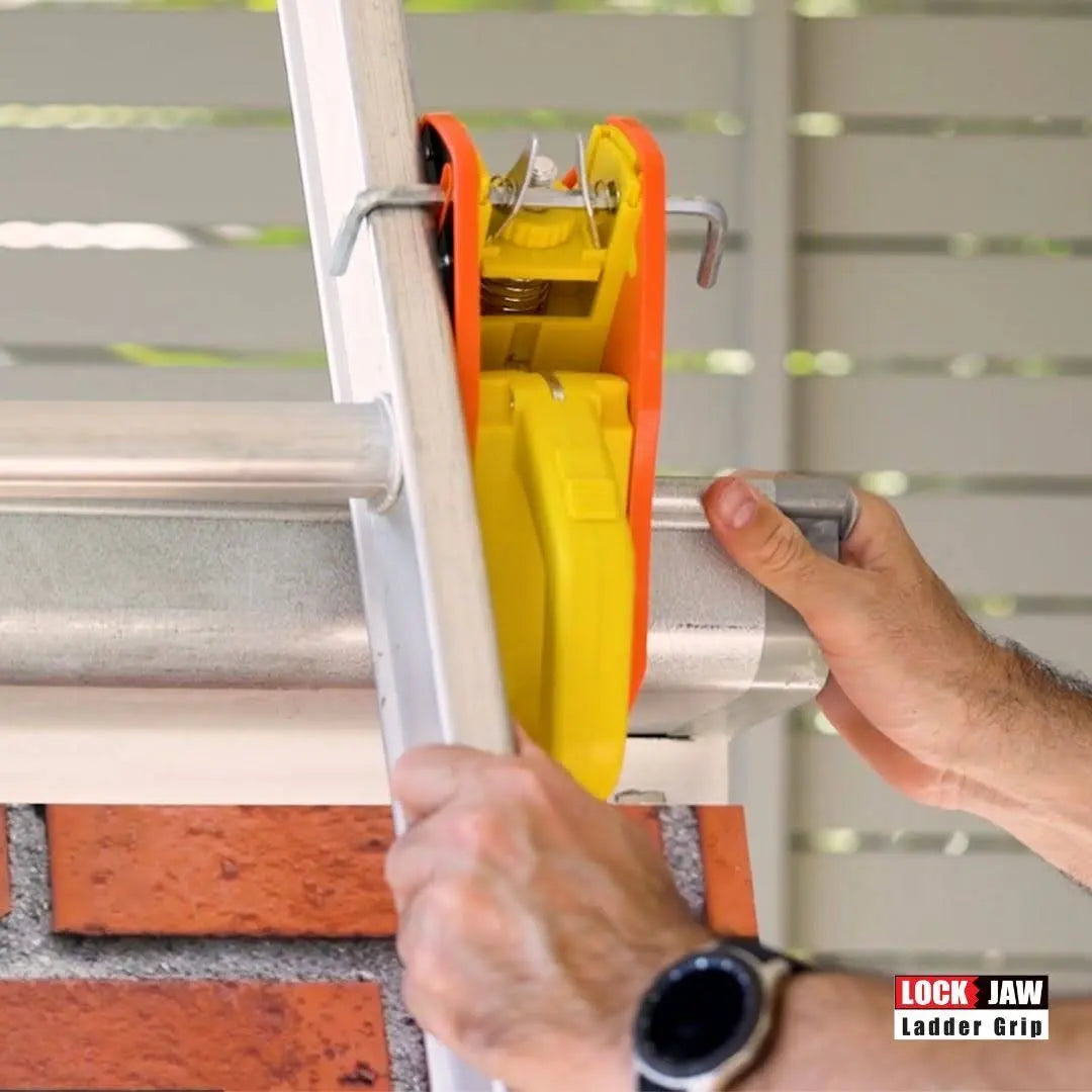 A hand holds a Lock Jaw Ladder Grip attached to a ladder.
