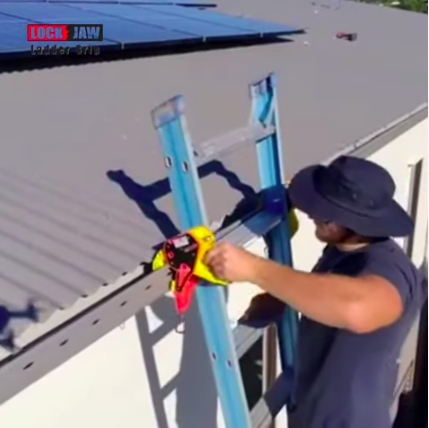 A man wearing a hat is securing a ladder to a roof using a Lock Jaw Ladder Grip.