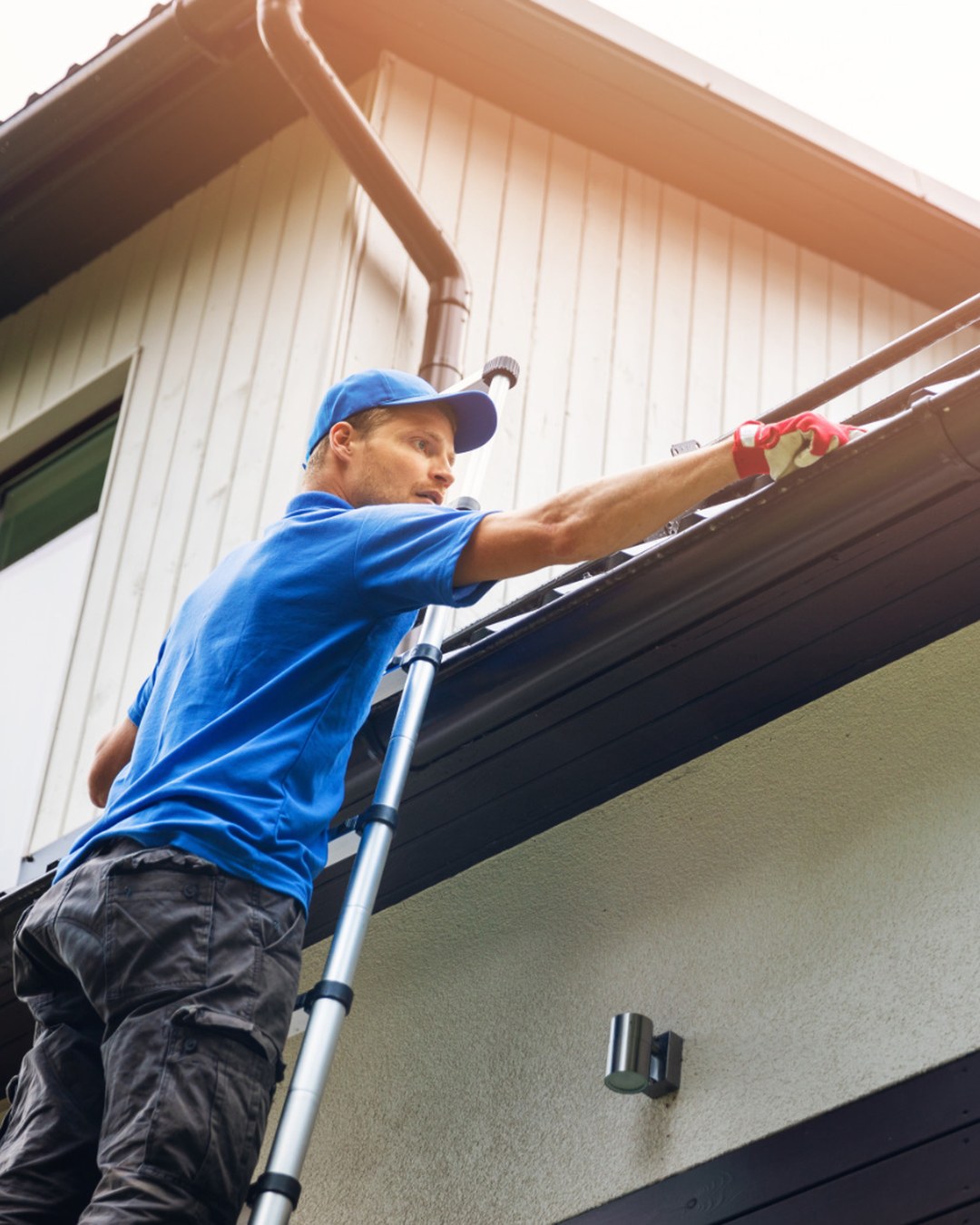 Gutter cleaner on a ladder clearing debris from a house gutter