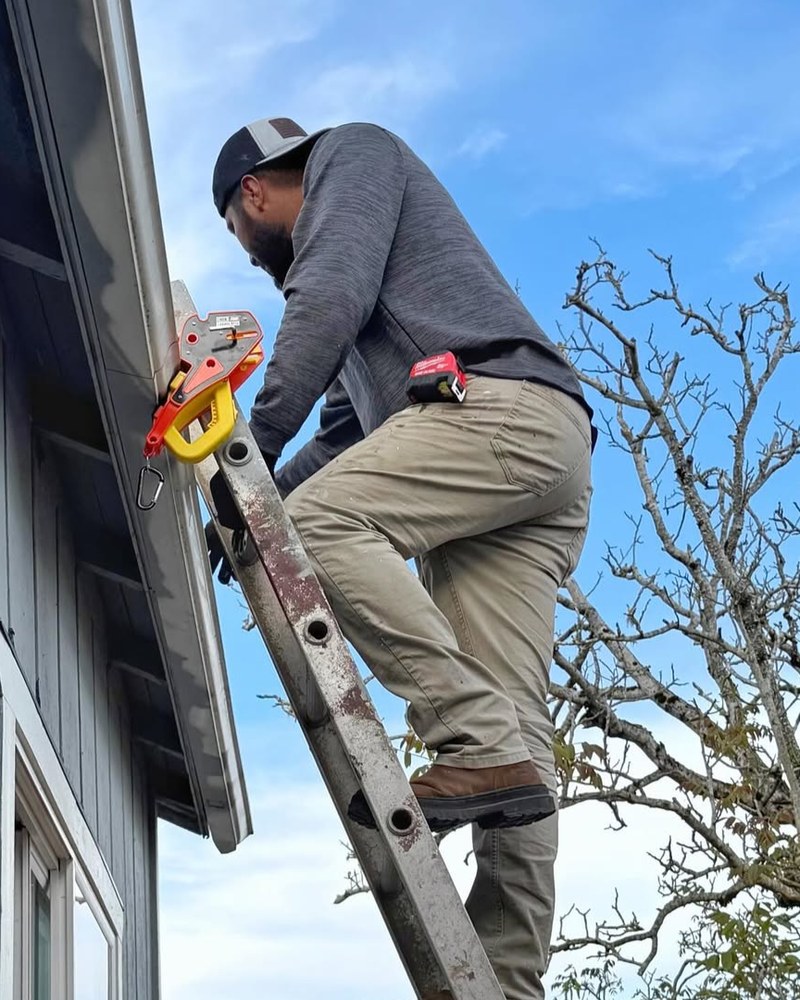 A roofer climbing an extension ladder fitted with a Lock Jaw Ladder Grip