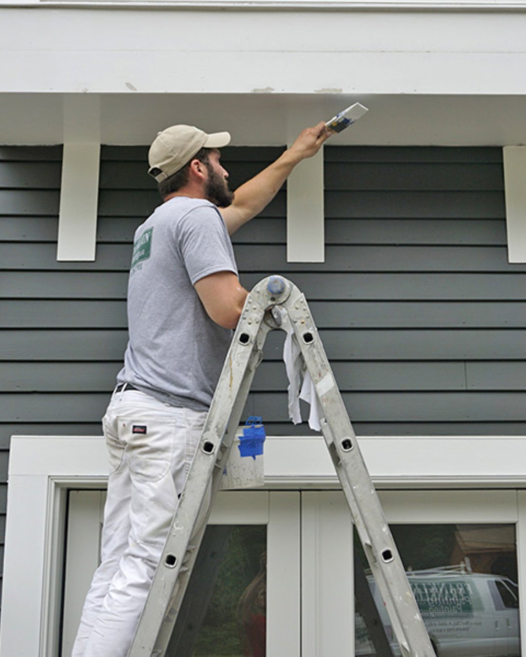 Painter on a ladder cutting in the eave line of a weatherboard house