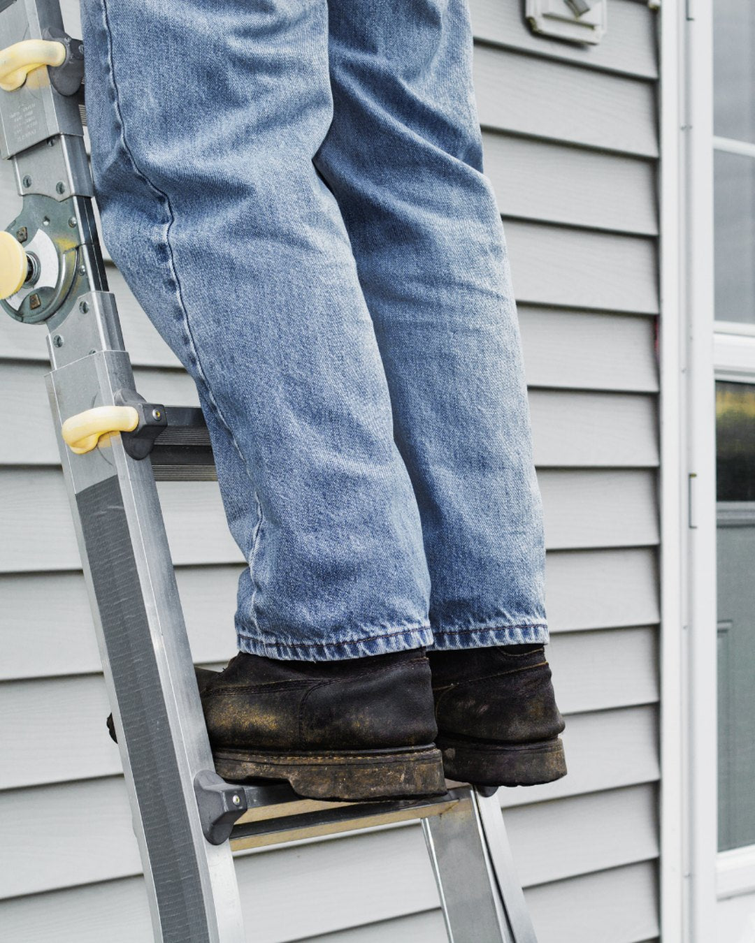 Technician climbing an extension ladder set against the wall of a house
