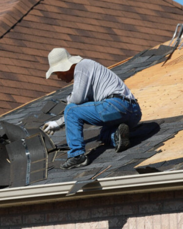 Roofer stripping shingles on a pitched roof at height